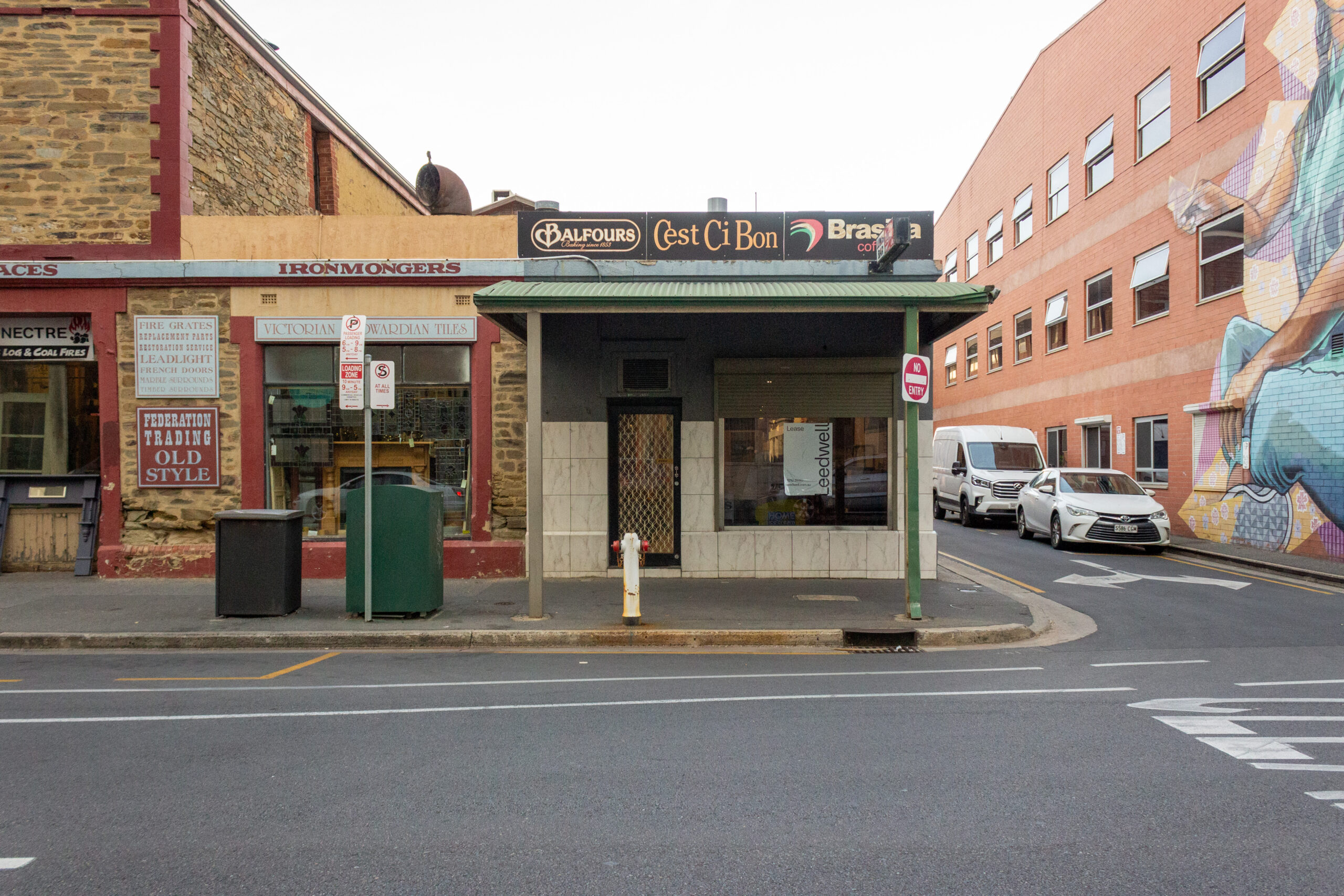 A front street view of the cafe located at 133 Waymouth Street, Adelaide. The facade includes signage for "Balfours," "C’est Ci Bon," and "Brasilia Coffee." Adjacent to the cafe is an ironmonger's shop "Federation Trading".