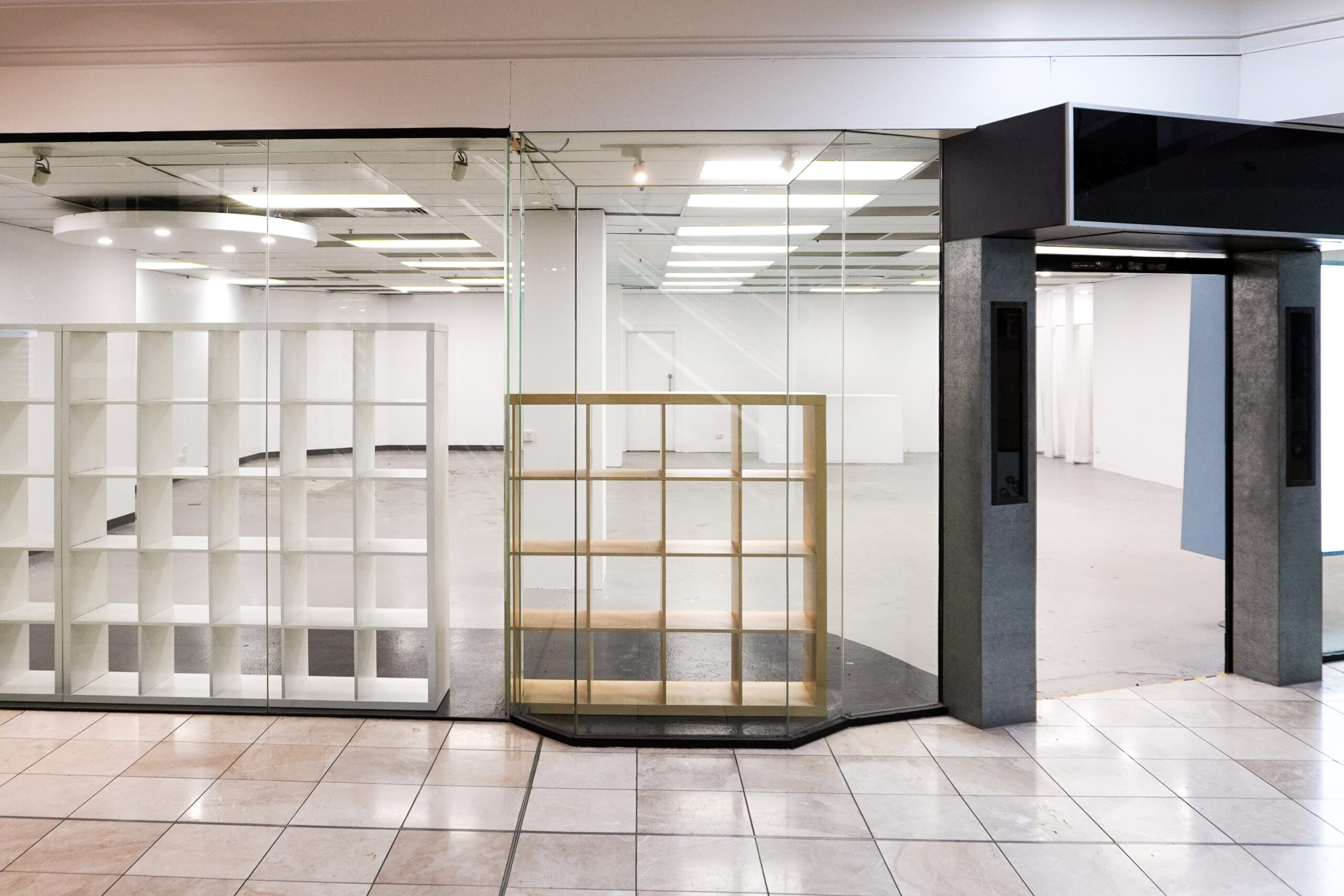 View of Shop 2.13 from outside the space, showing tiled floor, black-framed entrance and display boxes.