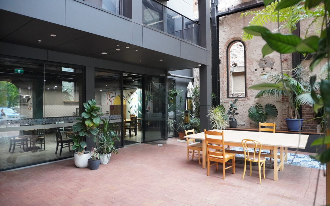 Cafe atrium showing paved courtyard, tables and seats, plants and cafe entrance.