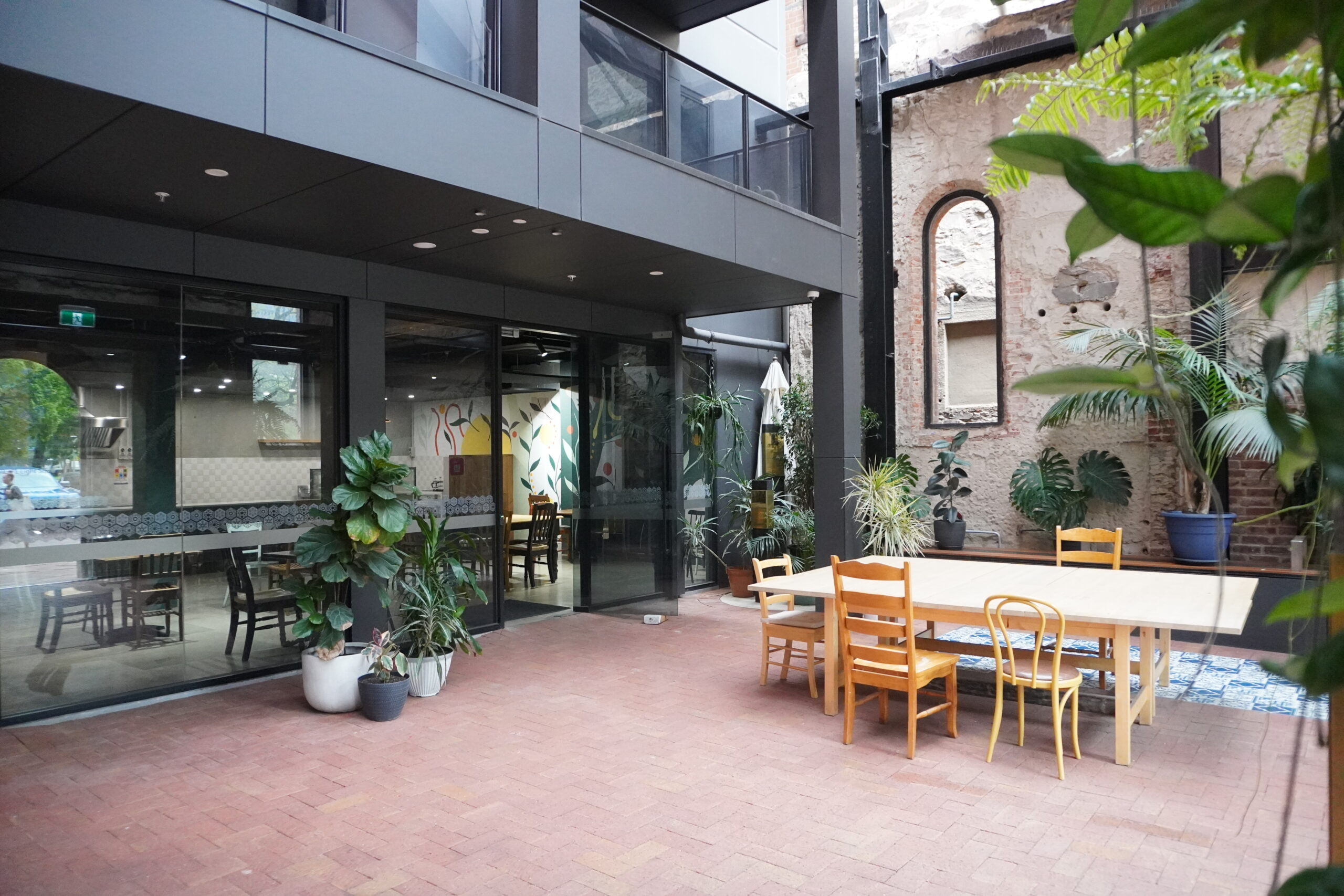 Cafe atrium showing paved courtyard, tables and seats, plants and cafe entrance.