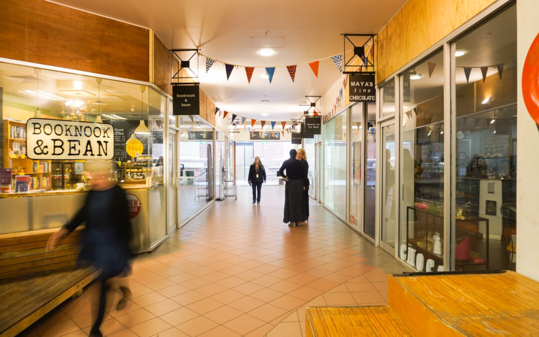 Inside Topham Mall, showing two people talking, bunting hanging overhead, and surrounding businesses.