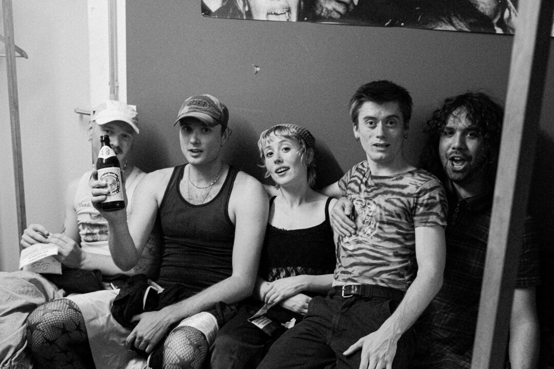 Black and white photo of five band members looking relaxed sitting backstage.