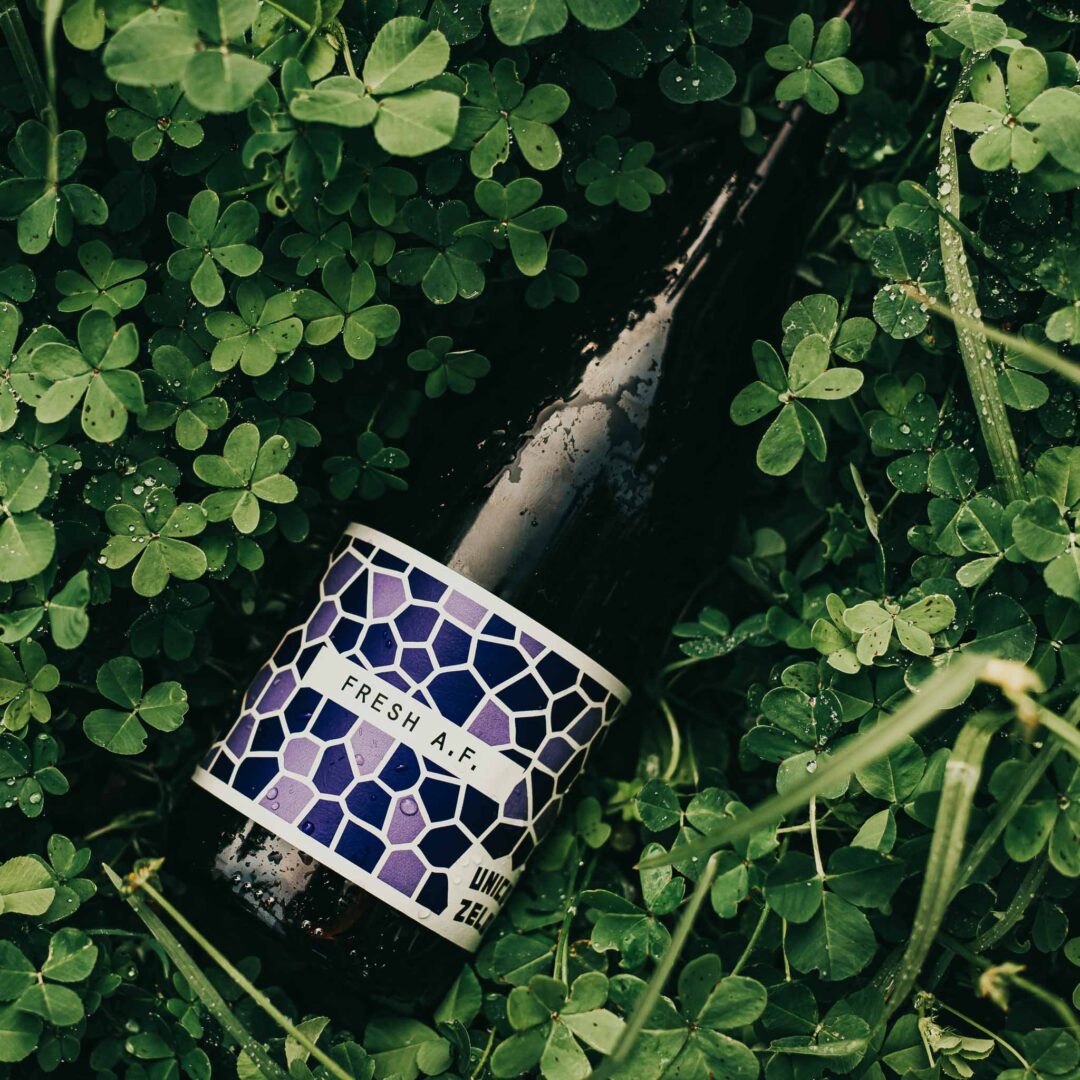 Dark bottle of Fresh AF wine nestled among green clovers.