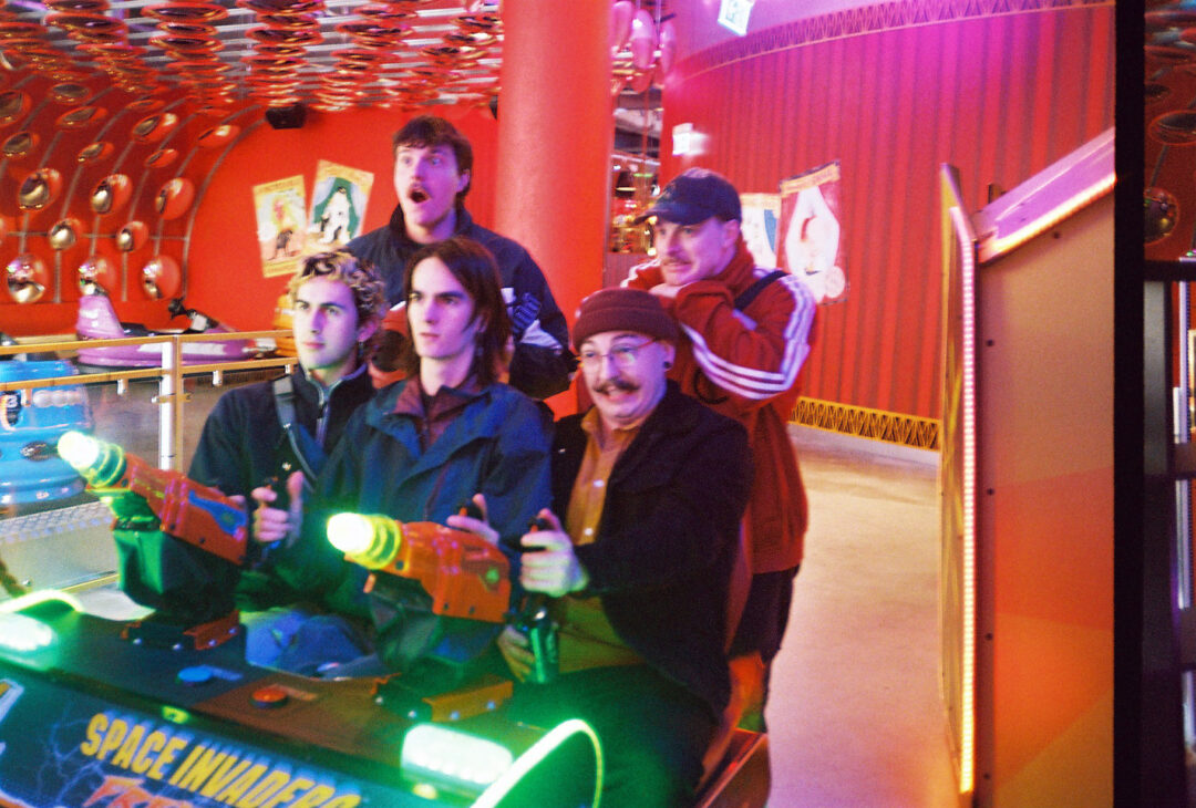 Five members of band playing an arcade game in a brightly lit space.