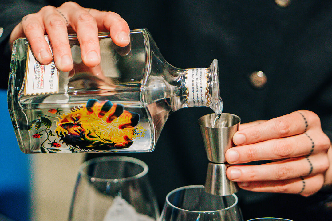 One hand pouring a square-shaped bottle of gin into a glass.