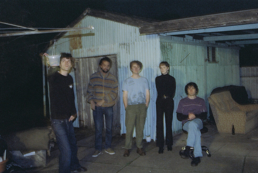 Five band members standing in a backyard at night, in front of a shed.