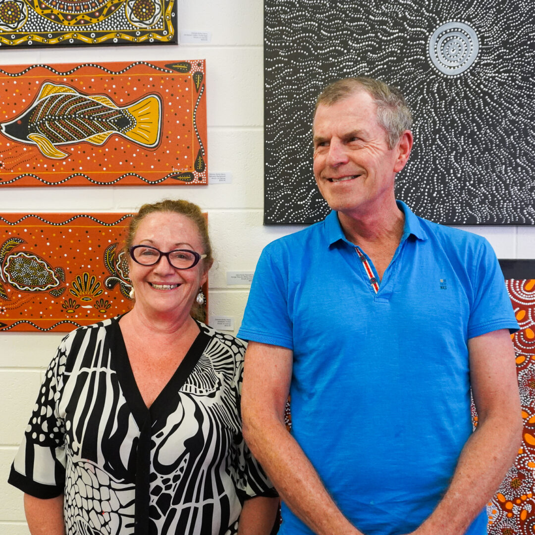 Owners Rowena and Paul smiling together, standing in front of a wall of Aboriginal artwork.