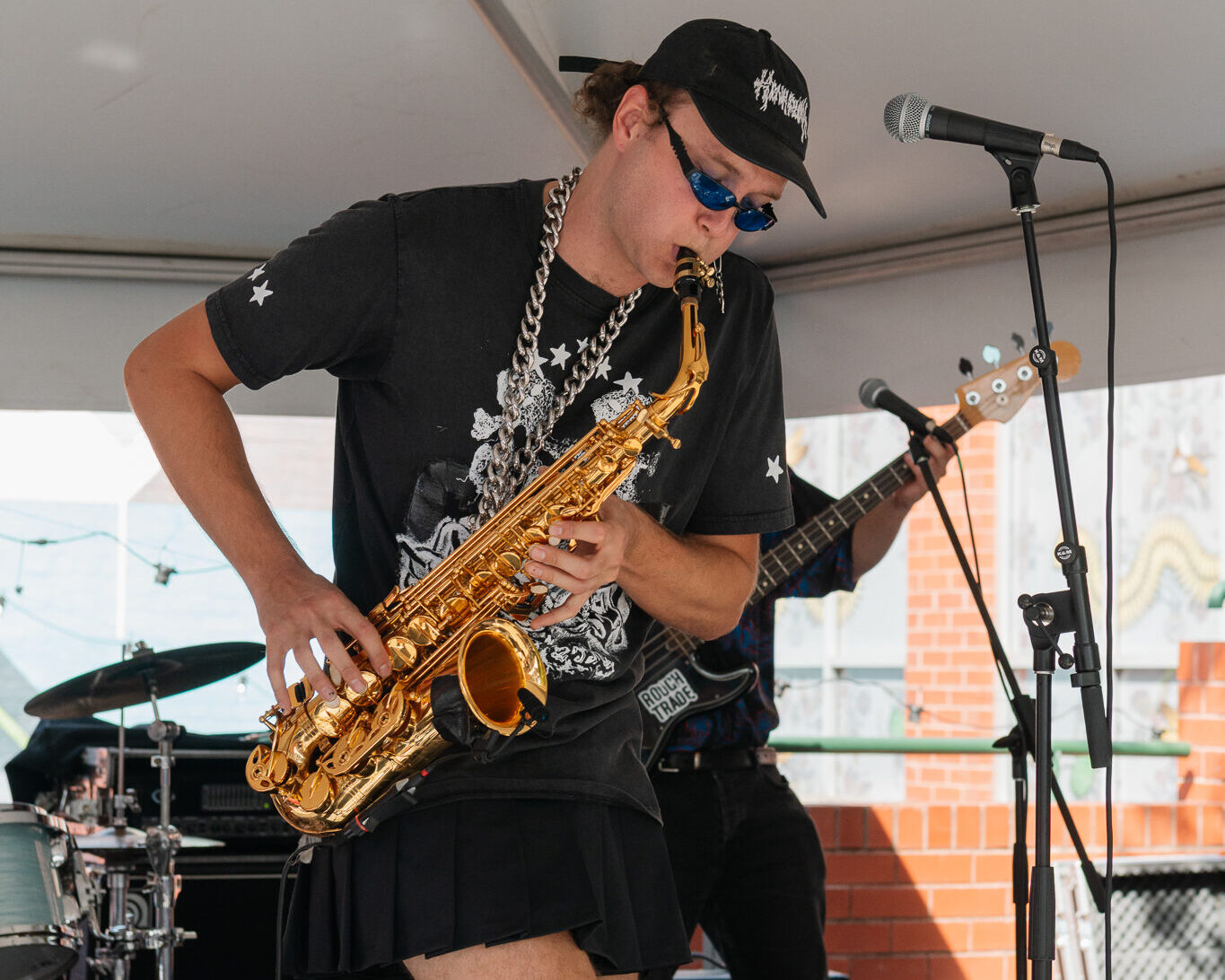 empty-threats Musician wearing all black, playing a saxophone and wearing a baseball cap.