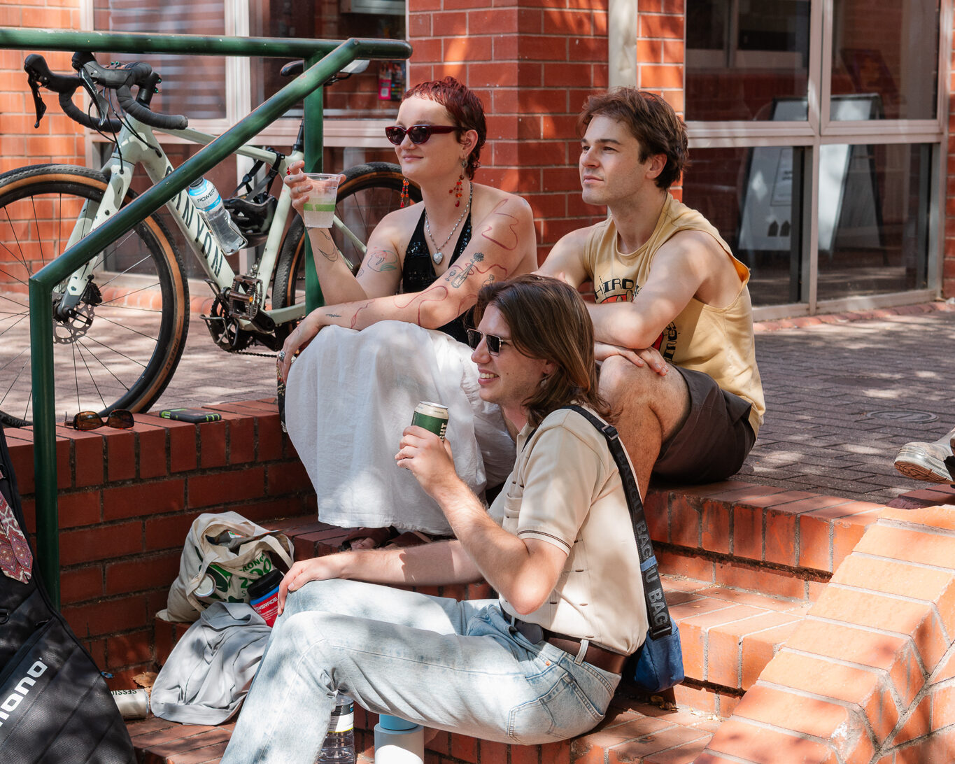 westbound-audience Three music fans sitting on brick stairs and watching the live music, with a bike in the background.