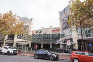 View of the shopping centre from O'Connell Street, showing parked cars, street and leafy trees.