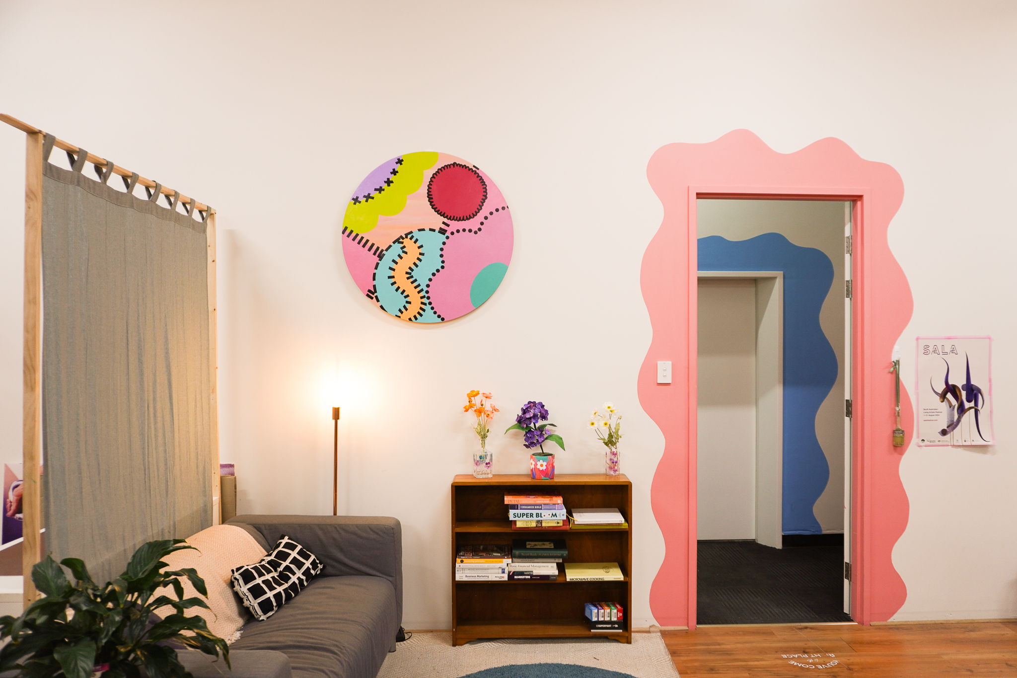 the-rundle-collective-06 Cosy common area, with couch and cushions, a small bookshelf and a funky pink door frame painted on the wall.