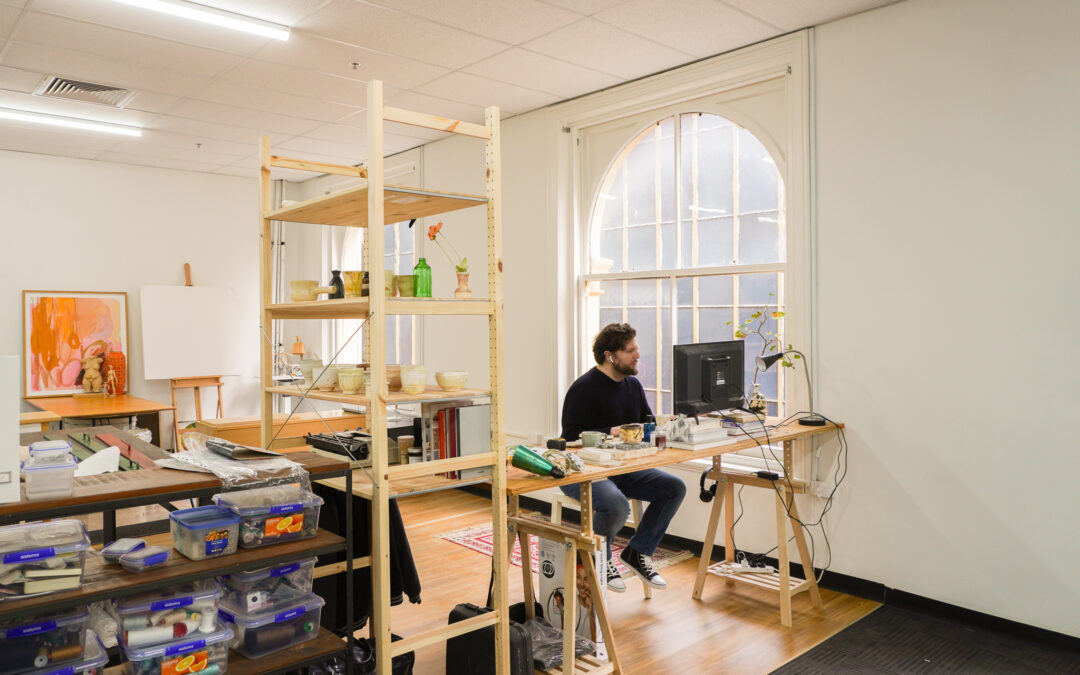 Artist working in a brightly lit space next to an arched window.