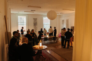 Venue with white walls, high ceilings and big windows, filled with people enjoying an event.