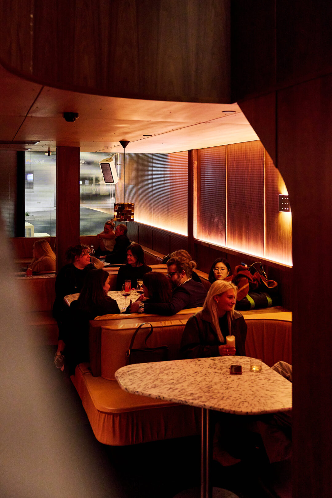 Wood panelled room with plush leather booths, showing people drinking cocktails.