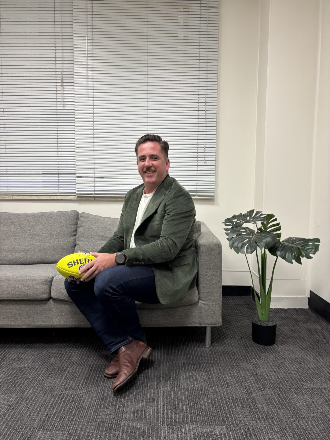 Owner Eamonn in his office, wearing a green jacket, sitting on a couch and holding a football.