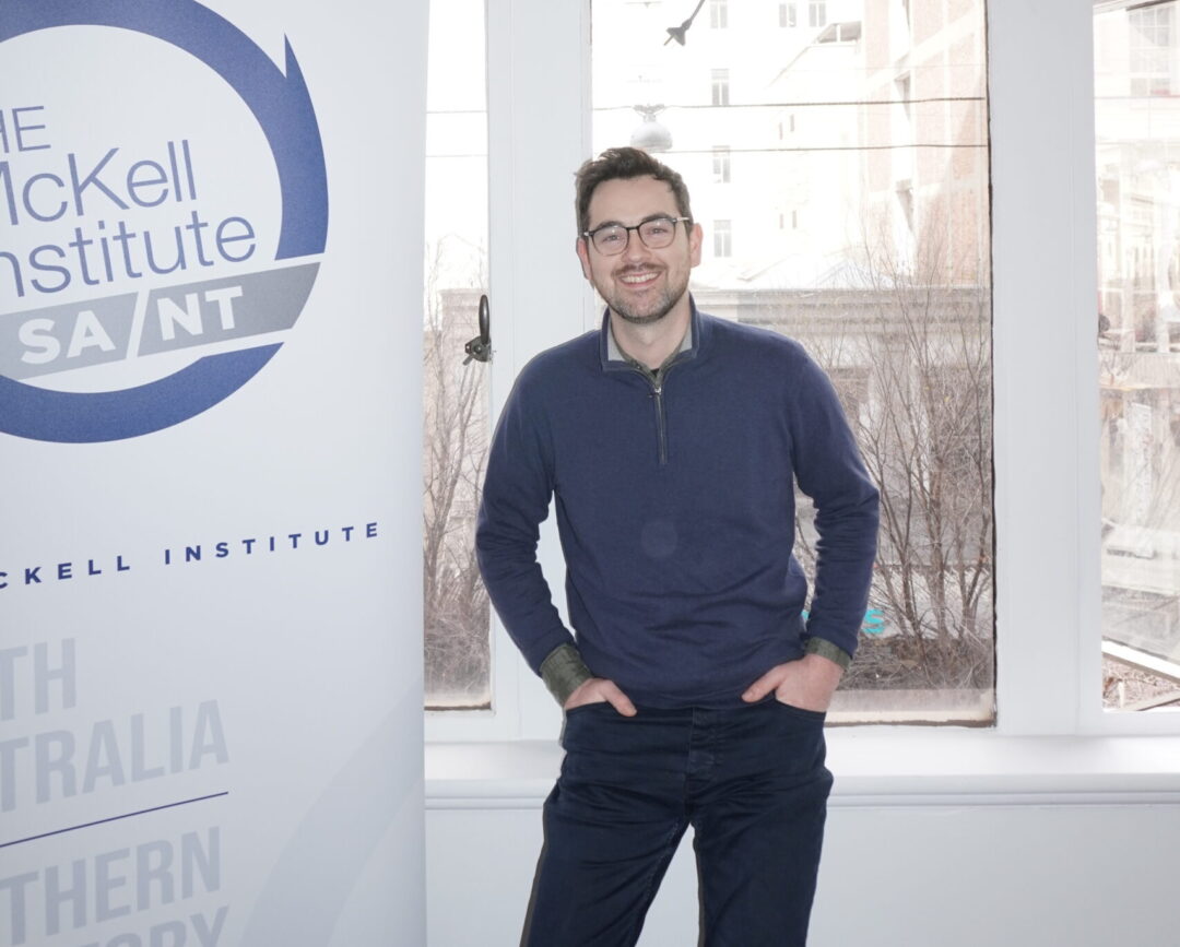 Smiling man in glasses standing in front of window.