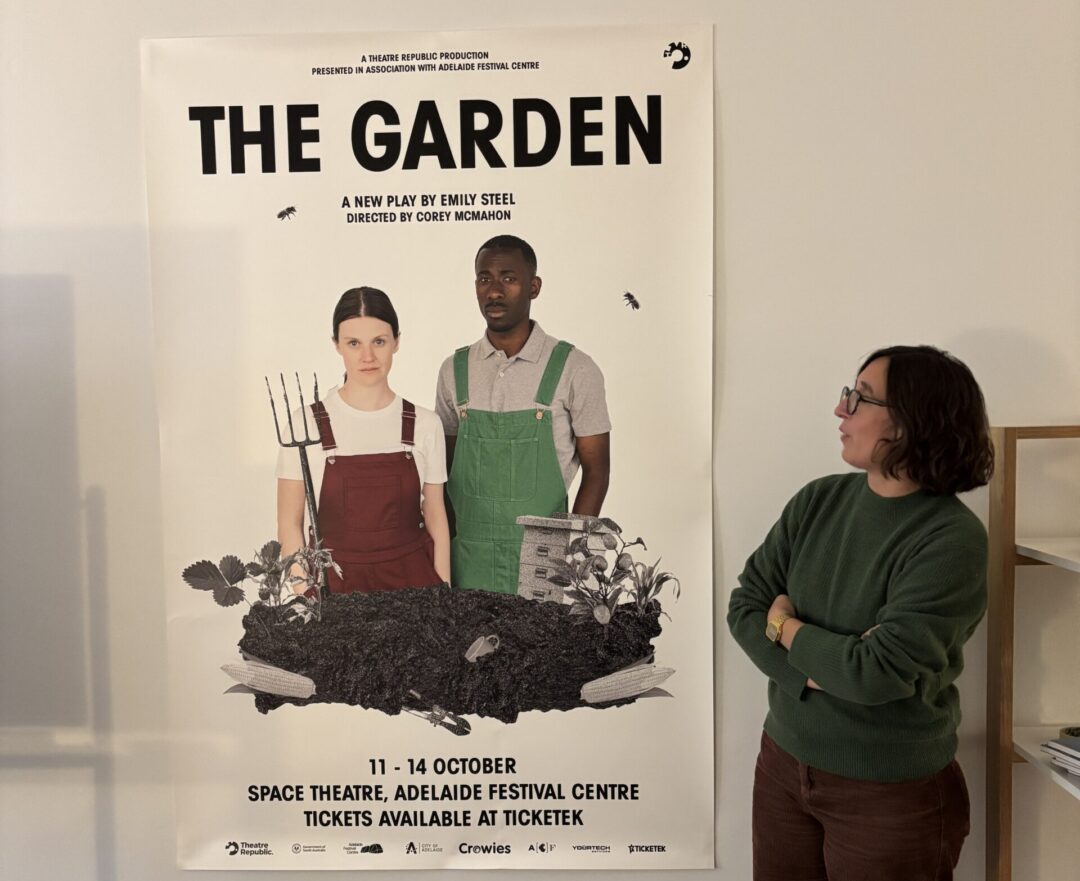 Woman in green jumper standing in front of theatre poster for a performance called "The Garden".