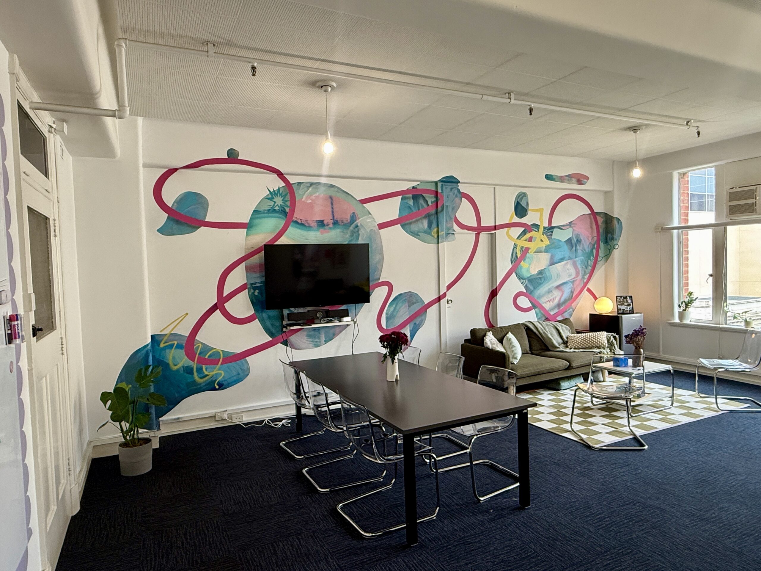 Office with dark floor panels, white wall, and a colourful mural by artist Dave Court at the rear.