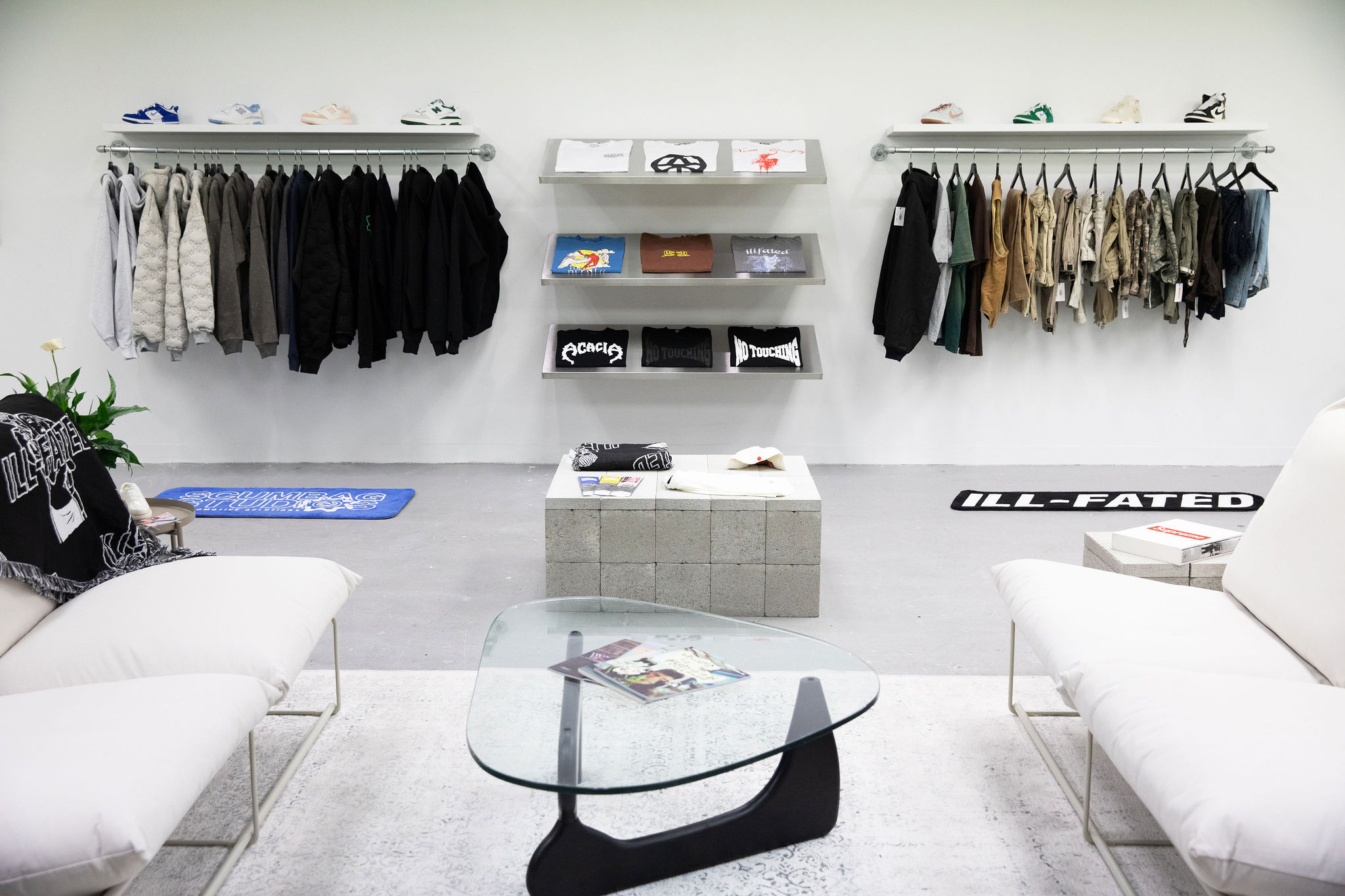White retail space with glass coffee table and clothing racks on rear wall.