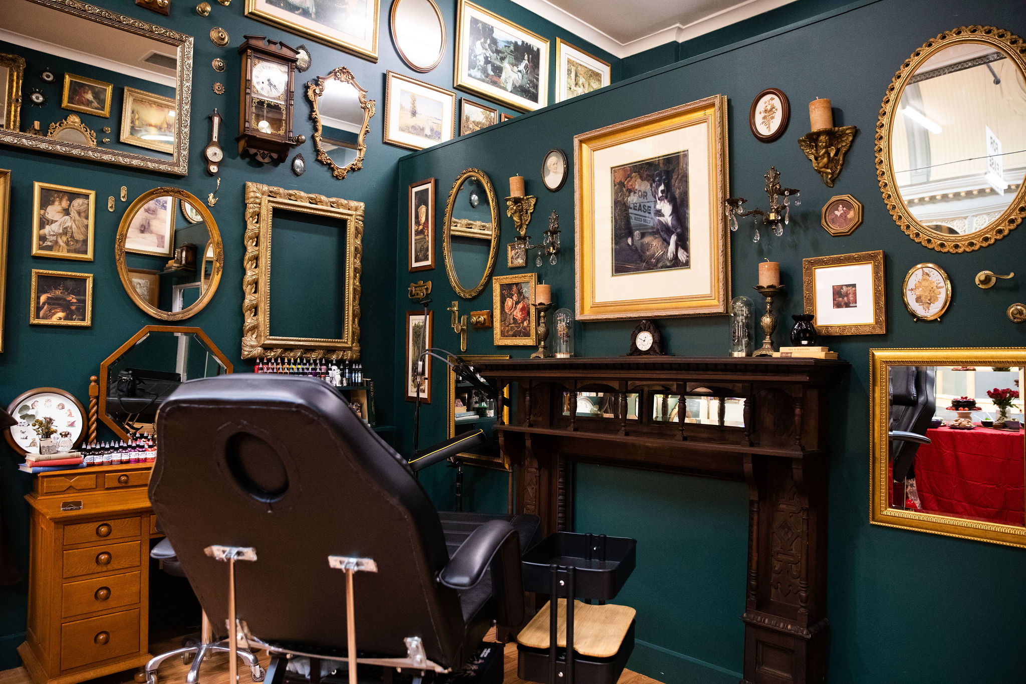 Tattoo studio with chair in foreground and lots of framed pictures on the green walls.