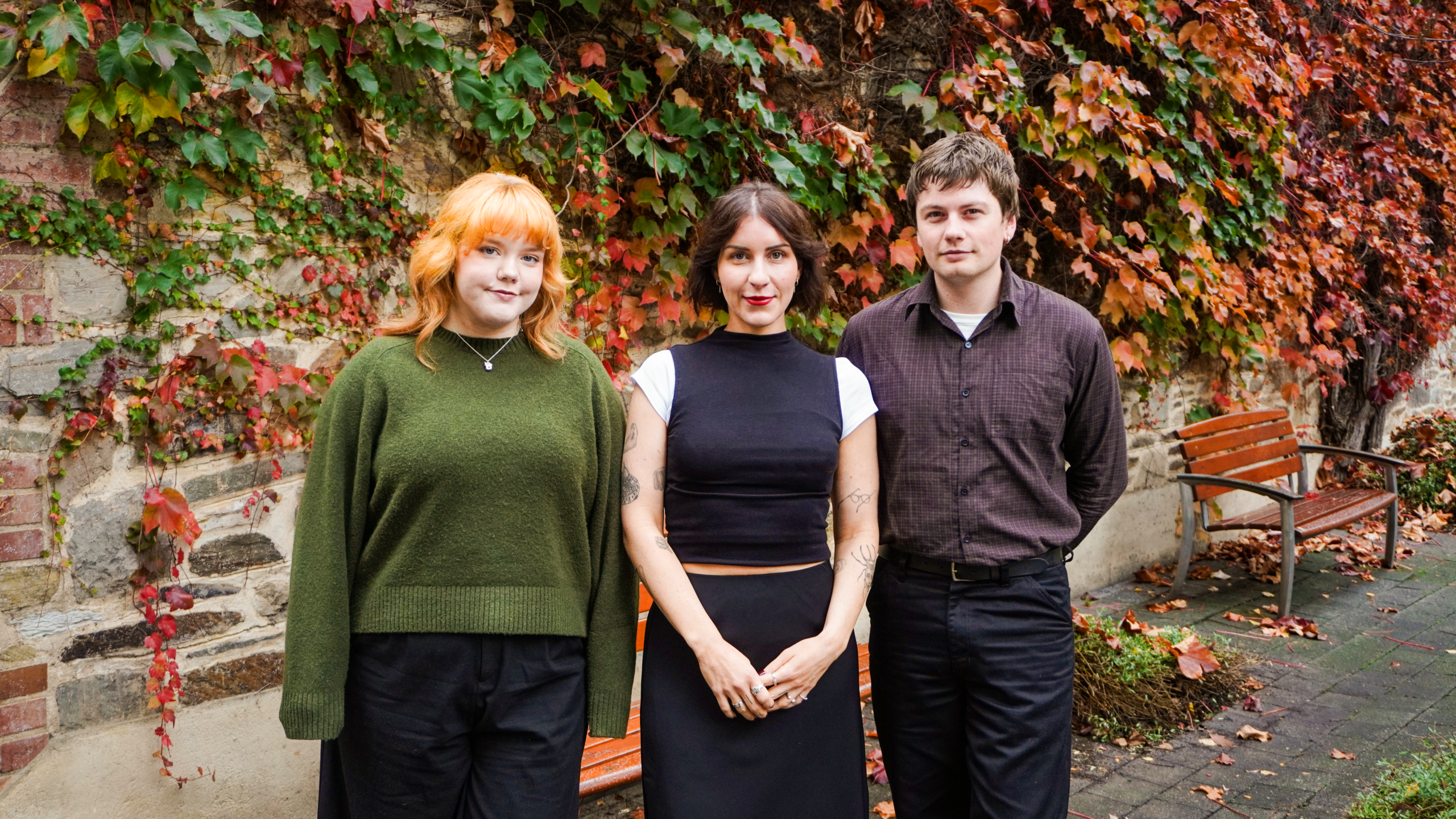 The three staff of Renew Adelaide standing in front of an Autumnal leafy brick wall.