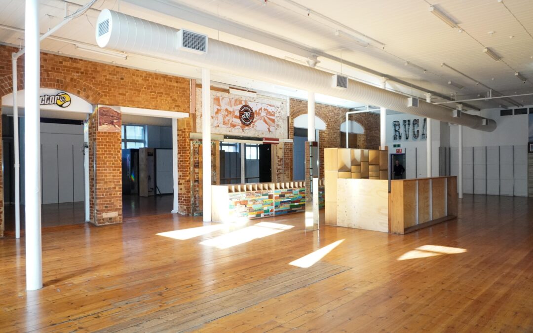 Large open-plan commercial space with polished timber floors, exposed red brick walls, high ceilings and abundant natural light.
