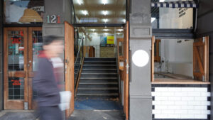 Front entrance to building with hold-in-the-wall kiosk to the right.